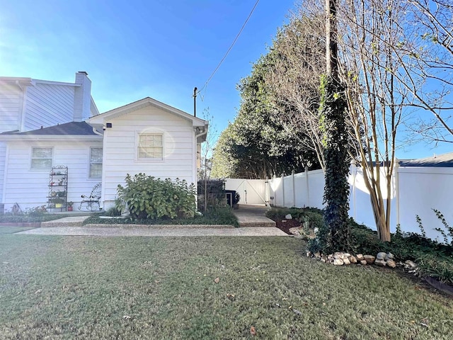 view of side of property featuring a gate, a lawn, a chimney, and fence