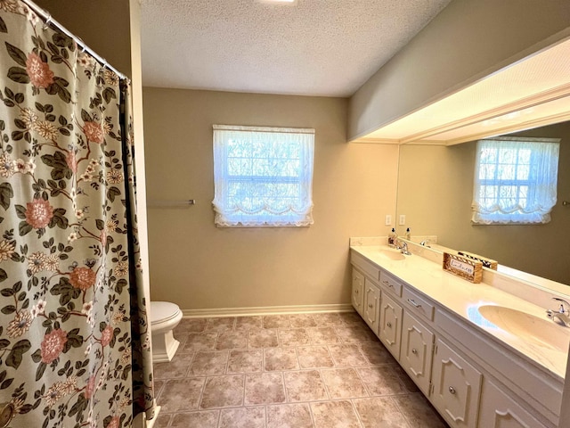 full bath featuring double vanity, baseboards, toilet, a textured ceiling, and a sink