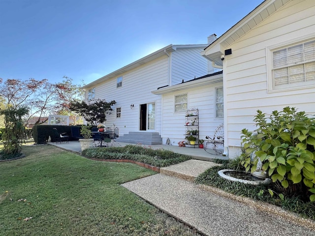 rear view of property with entry steps, a chimney, a lawn, and a patio