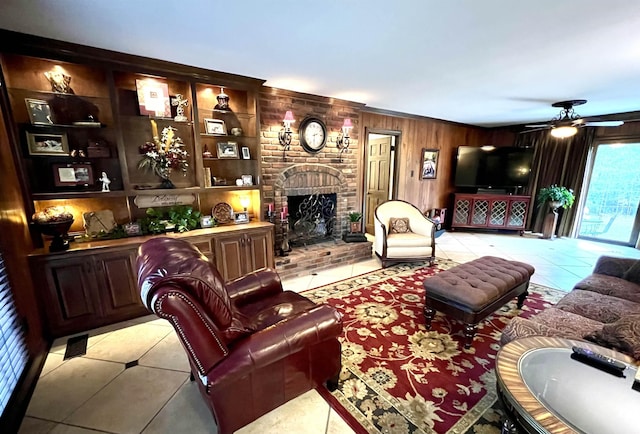 living area featuring light tile patterned floors, a brick fireplace, a ceiling fan, and wood walls