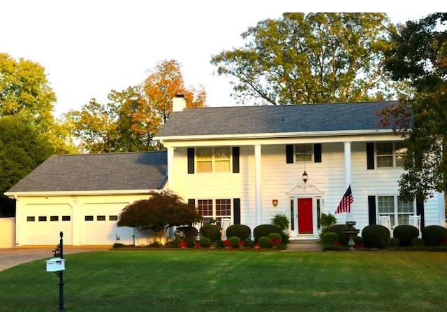 view of front of house with a front yard, driveway, a chimney, and an attached garage