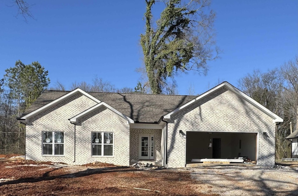 single story home featuring a garage, driveway, roof with shingles, and brick siding