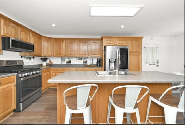 kitchen featuring hardwood / wood-style floors, a center island, sink, appliances with stainless steel finishes, and a breakfast bar area