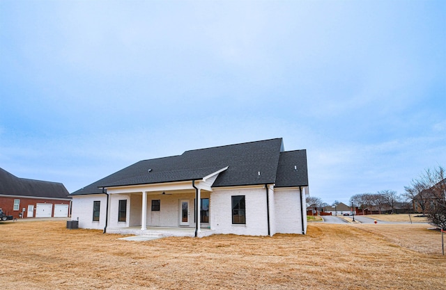 rear view of property featuring central AC unit, a lawn, a ceiling fan, roof with shingles, and a patio area