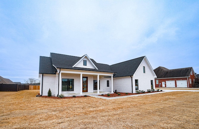 modern inspired farmhouse with covered porch, a garage, brick siding, fence, and a front yard