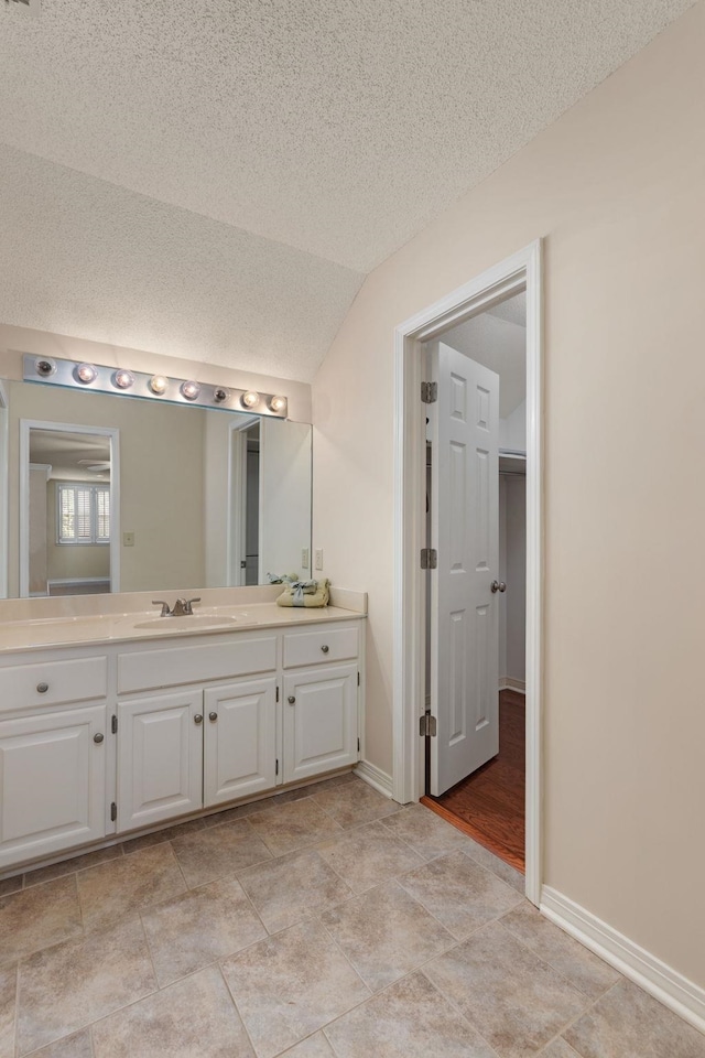  - bathroom featuring vanity, vaulted ceiling, baseboards, and a textured ceiling