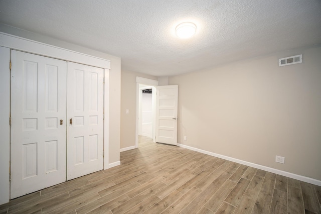 unfurnished bedroom with a textured ceiling, light hardwood / wood-style flooring, and a closet