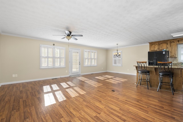 unfurnished living room featuring ceiling fan with notable chandelier, a healthy amount of sunlight, ornamental molding, and dark wood-type flooring