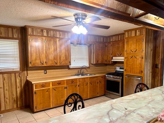 kitchen with sink, wooden walls, ceiling fan, a textured ceiling, and stainless steel range