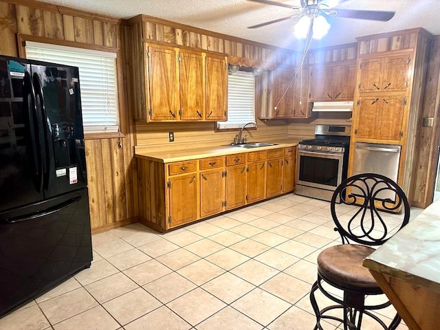 kitchen featuring black fridge, a textured ceiling, sink, stainless steel range oven, and wood walls