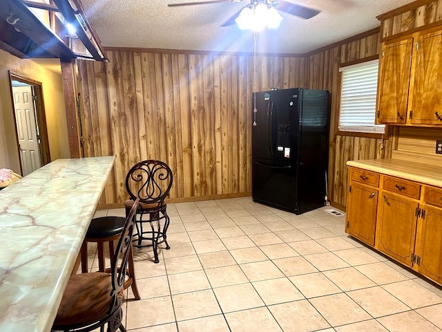 kitchen featuring a textured ceiling, black fridge, ceiling fan, and wood walls