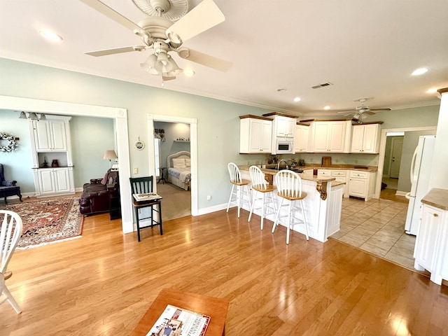 kitchen featuring a breakfast bar, white cabinetry, kitchen peninsula, white appliances, and light hardwood / wood-style flooring