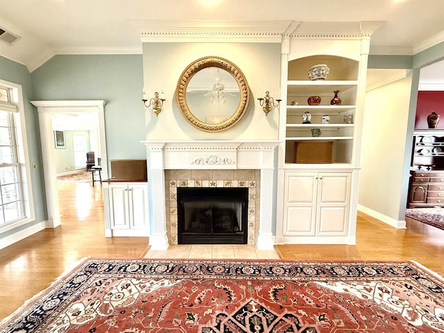 living room featuring vaulted ceiling, a fireplace, ornamental molding, light wood-type flooring, and built in shelves