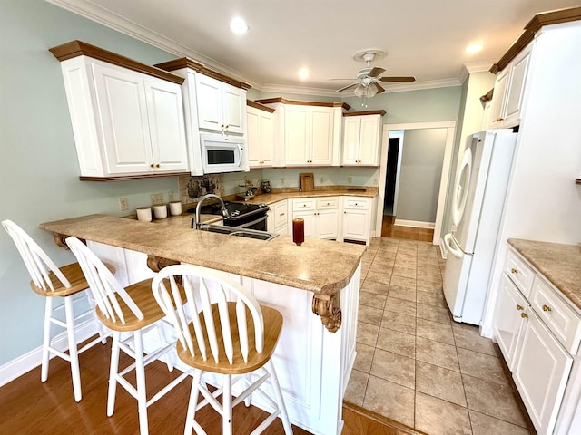 kitchen with white appliances, kitchen peninsula, sink, and a breakfast bar area