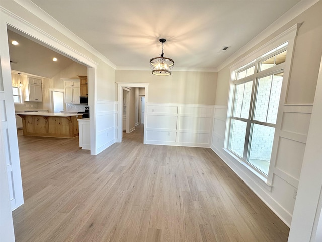 unfurnished dining area featuring ornamental molding, a chandelier, and light hardwood / wood-style flooring