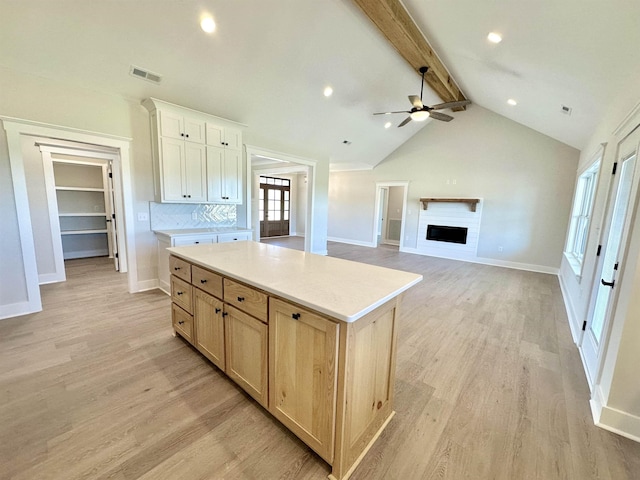 kitchen with a kitchen island, ceiling fan, light brown cabinets, beam ceiling, and light hardwood / wood-style flooring