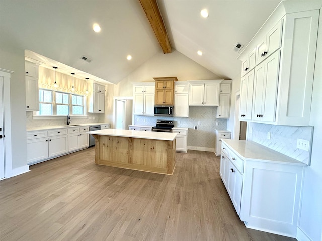 kitchen with appliances with stainless steel finishes, decorative light fixtures, beamed ceiling, white cabinets, and a center island