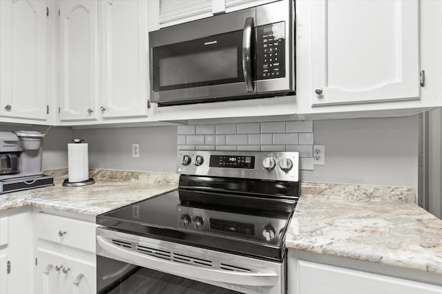  - kitchen featuring appliances with stainless steel finishes, white cabinets, tasteful backsplash, and light stone counters