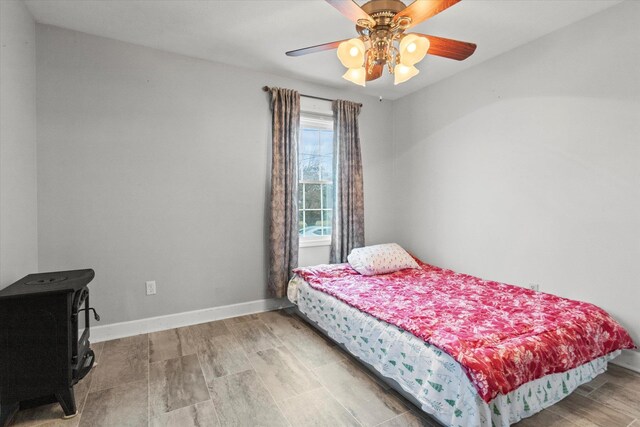  - bedroom featuring a wood stove, baseboards, and ceiling fan
