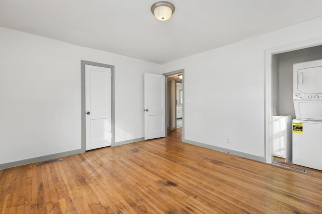 unfurnished bedroom featuring light hardwood / wood-style floors and stacked washing maching and dryer