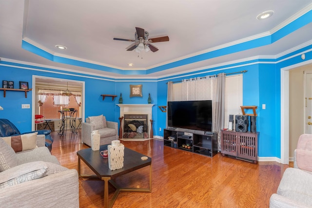  - living area with a raised ceiling, ceiling fan, wood finished floors, and ornamental molding