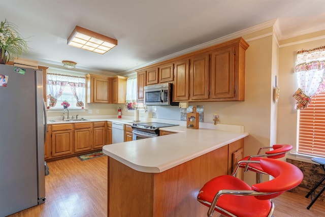  - kitchen with appliances with stainless steel finishes, ornamental molding, light wood-type flooring, a peninsula, and light countertops