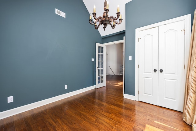 unfurnished bedroom featuring hardwood / wood-style flooring, high vaulted ceiling, a closet, and a notable chandelier