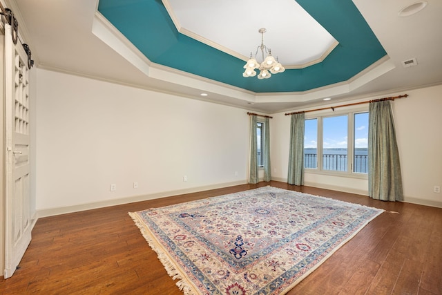 interior space featuring a raised ceiling, dark wood-type flooring, crown molding, a water view, and an inviting chandelier