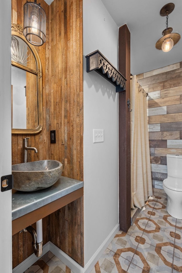 bathroom with a shower with shower curtain, toilet, sink, and wooden walls