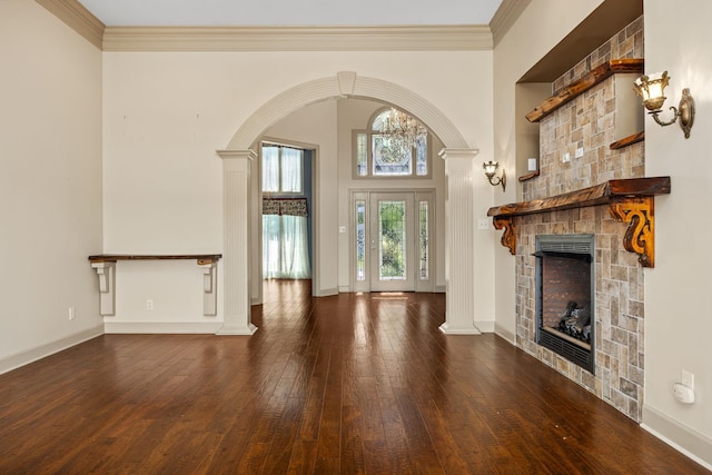 unfurnished living room featuring a fireplace, decorative columns, dark wood-type flooring, and crown molding