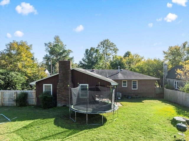 back of property featuring a trampoline and a lawn