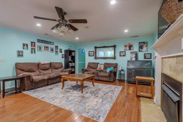 living room with a tile fireplace, ceiling fan, and light wood-type flooring