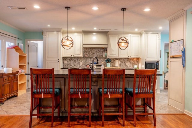 bar with pendant lighting, light wood-type flooring, ornamental molding, and dark stone countertops