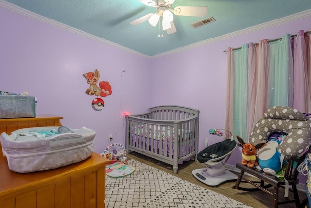 bedroom featuring ceiling fan, wood-type flooring, a crib, and crown molding