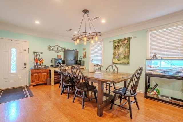 dining area with light wood-type flooring, ornamental molding, and a chandelier