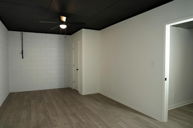 spare room featuring baseboards, concrete block wall, a ceiling fan, and wood finished floors