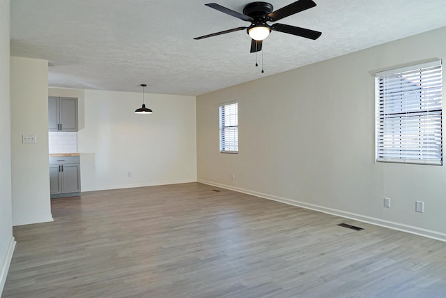 empty room featuring light wood-style flooring, baseboards, visible vents, and a textured ceiling