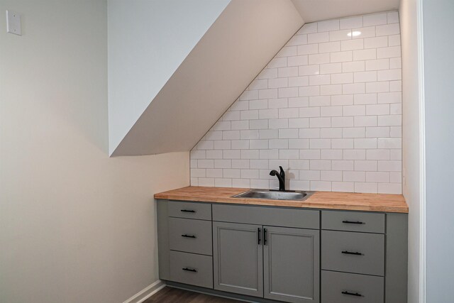 bar featuring baseboards, dark wood finished floors, lofted ceiling, a sink, and backsplash