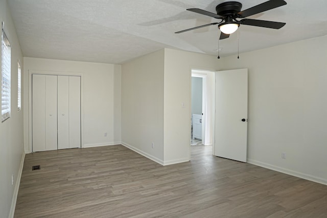 unfurnished bedroom featuring visible vents, a textured ceiling, baseboards, and wood finished floors