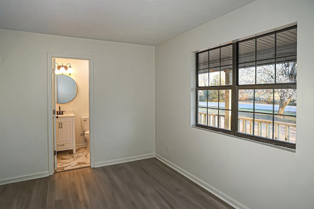 unfurnished bedroom with a sink, baseboards, dark wood-type flooring, and ensuite bath