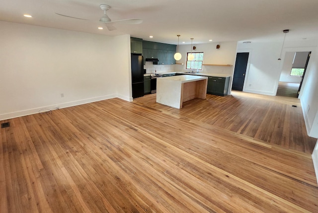 kitchen with black fridge, ceiling fan, light hardwood / wood-style flooring, a center island, and hanging light fixtures