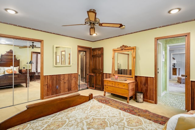 carpeted bedroom with ceiling fan, crown molding, wooden walls, and a closet