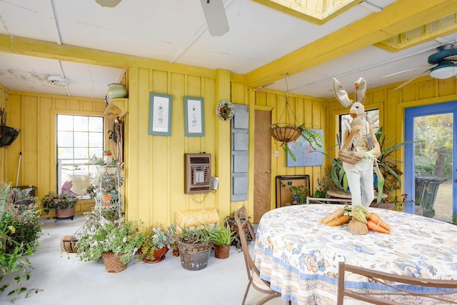 dining area featuring concrete flooring, heating unit, ceiling fan, and wood walls