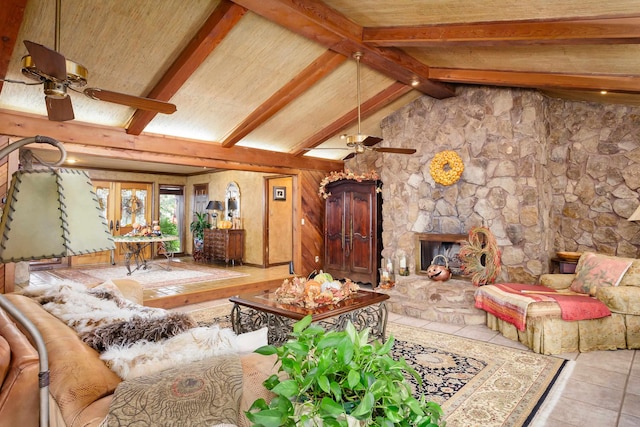 living room featuring ceiling fan, vaulted ceiling with beams, a stone fireplace, wooden walls, and light tile patterned floors