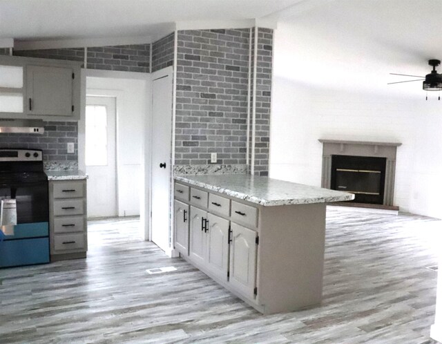  - kitchen featuring brick wall, light wood-style flooring, ceiling fan, extractor fan, and black range with electric cooktop