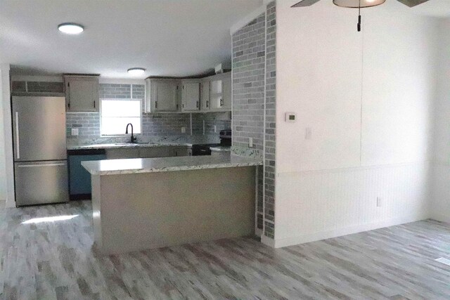  - kitchen featuring decorative backsplash, appliances with stainless steel finishes, a peninsula, and light wood finished floors