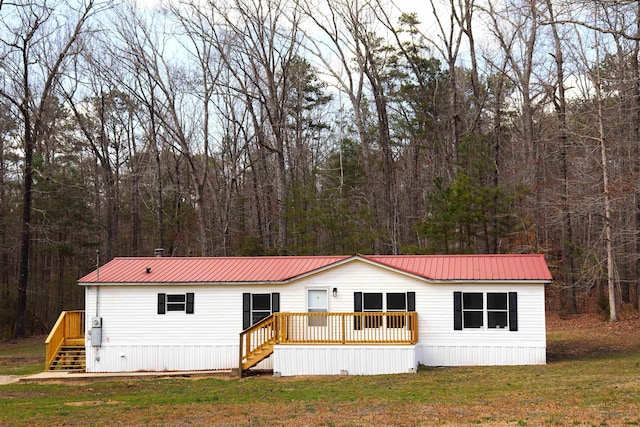 manufactured / mobile home featuring metal roof, a view of trees, a front lawn, and stairway