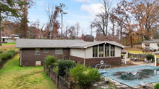 rear view of property featuring a covered pool, a patio area, and a lawn