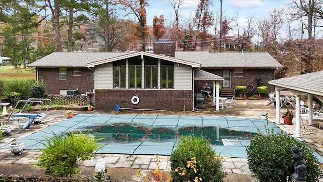 rear view of property featuring a patio and a covered pool