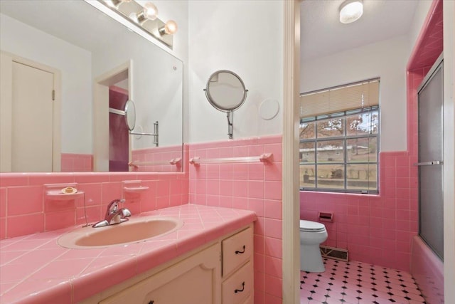 full bathroom with vanity, bath / shower combo with glass door, tile walls, and toilet